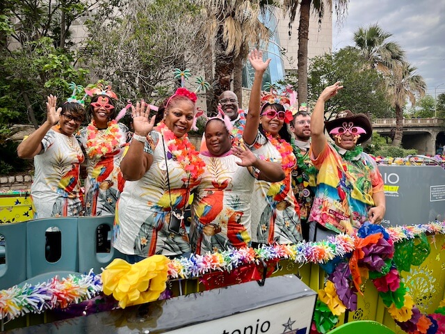 A group of adults waves from a river barge during a Fiesta parade in San Antonio