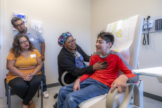 A young person being examined by a medical provider while their parents watch.