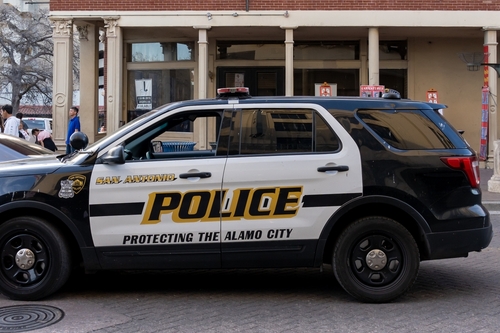 A San Antonio Police car parked on a street in an urban area.