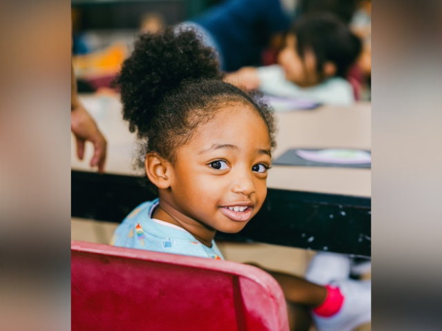 A young person looks over their shoulder at the camera while sitting at table with other children.